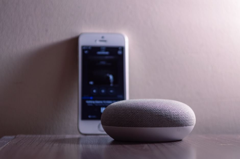 A modern smart speaker and smartphone on a wooden table