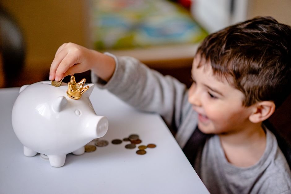 Young boy putting a coin in his piggy bank as part of saving for grandchild college