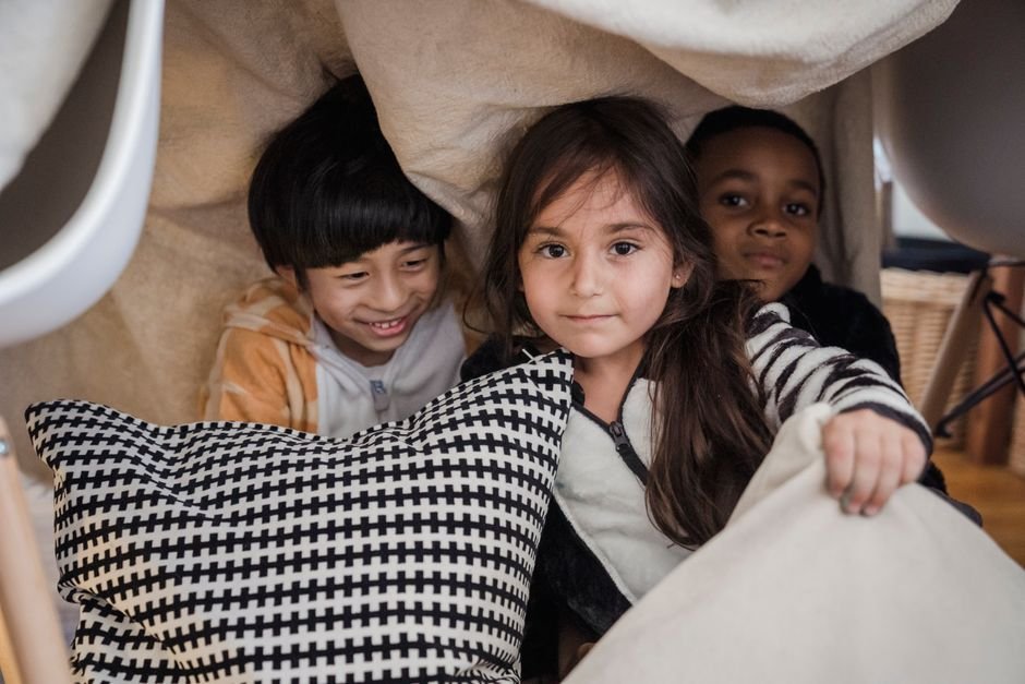 Three children doing indoor activities for grandkids in a cozy blanket fort