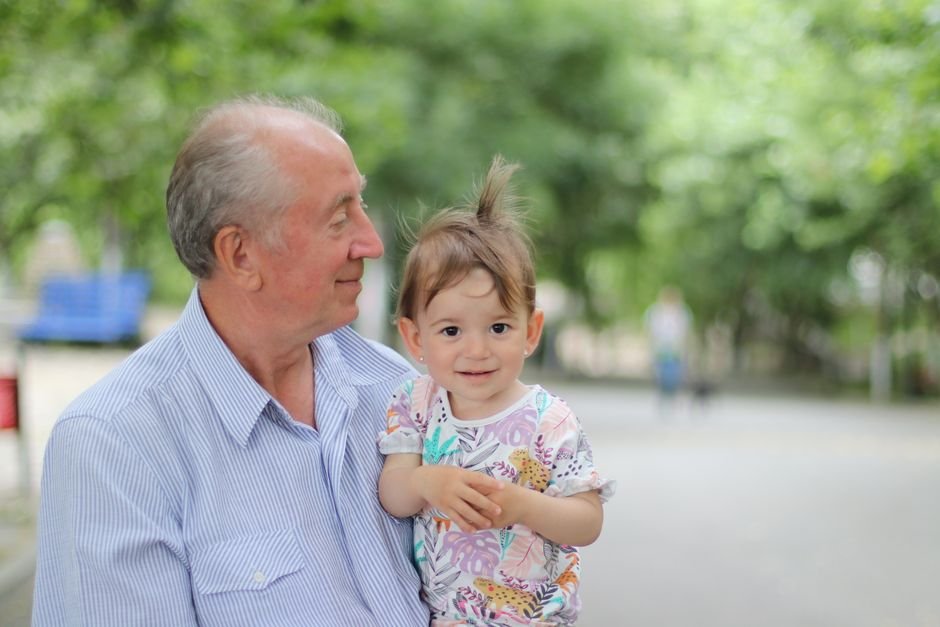 A grandfather holding his grandchild in a sunny park