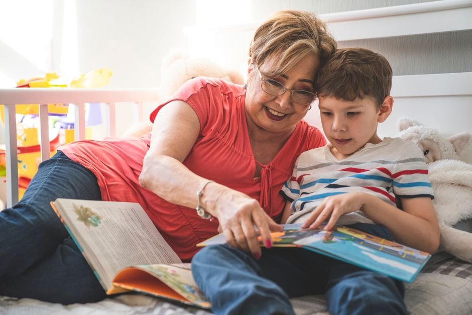 Elderly woman reading a book with her grandson on a cozy bed