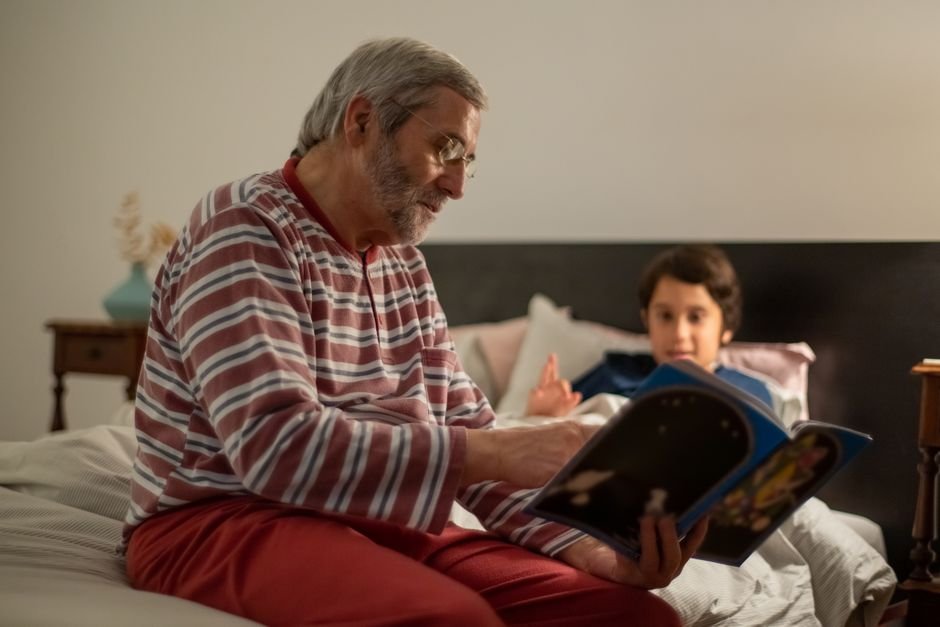 A senior man reads a bedtime story to his grandchild in a cozy indoor setting